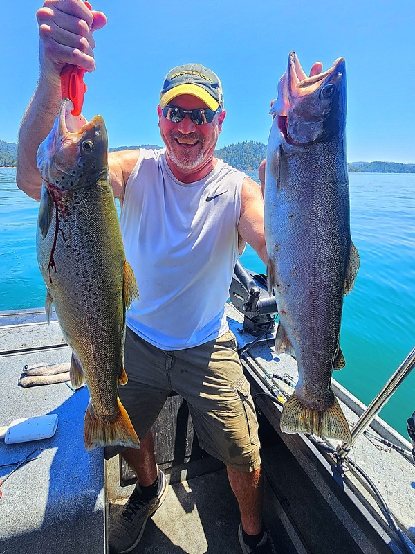 Angler holding up two large Shasta Lake trout on a bright summer day on the water