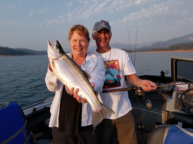 Two anglers holding a Shasta Lake trout at sunset with the Northern California hills behind them